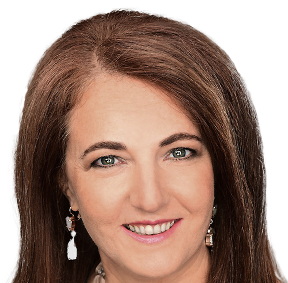 A woman smiles into the camera. She has auburn coloured hair and green eyes. She is wearing pink lipstick, silver dangle earrings and a silver necklace.